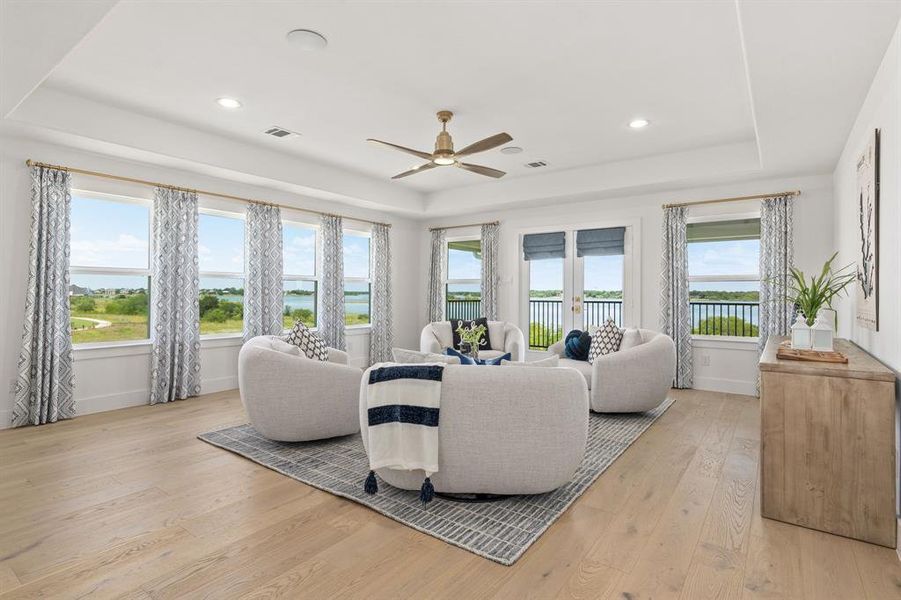 Living area with a raised ceiling, light wood-type flooring, a water view, ceiling fan, and recessed lighting Living area with a raised ceiling, light wood-type flooring, a water view, ceiling fan, and recessed lighting