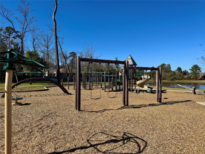 Playground with swings, a slide, and climbing structures, set on a mulch-covered ground. It's located in a scenic area with a pond and surrounded by trees, providing a family-friendly outdoor space. Playground with swings, a slide, and climbing structures, set on a mulch-covered ground. It's located in a scenic area with a pond and surrounded by trees, providing a family-friendly outdoor space.