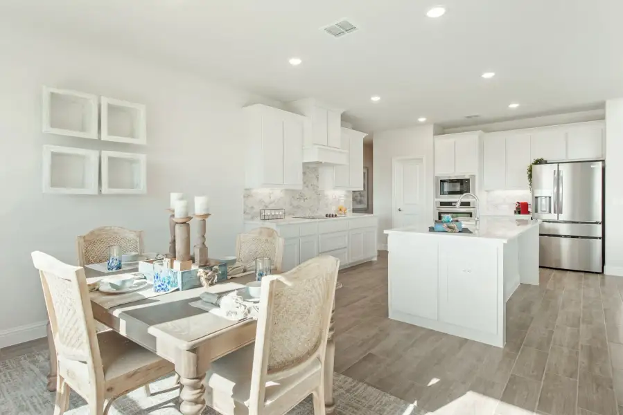 Open-concept kitchen and dining area with white cabinets, center island, stainless appliances, and wood-look floors