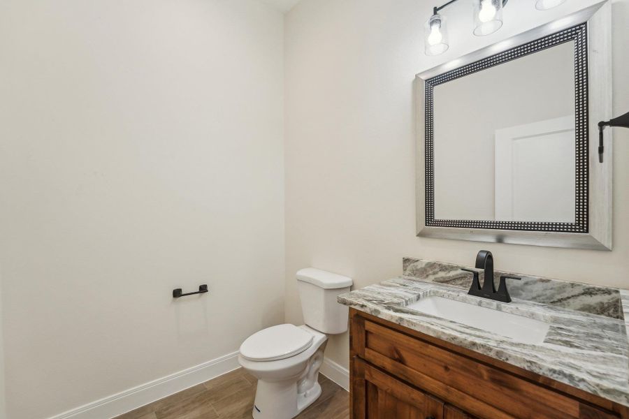 Half bath featuring baseboards, toilet, wood plank tile floor, and vanity Half bath featuring baseboards, toilet, wood plank tile floor, and vanity