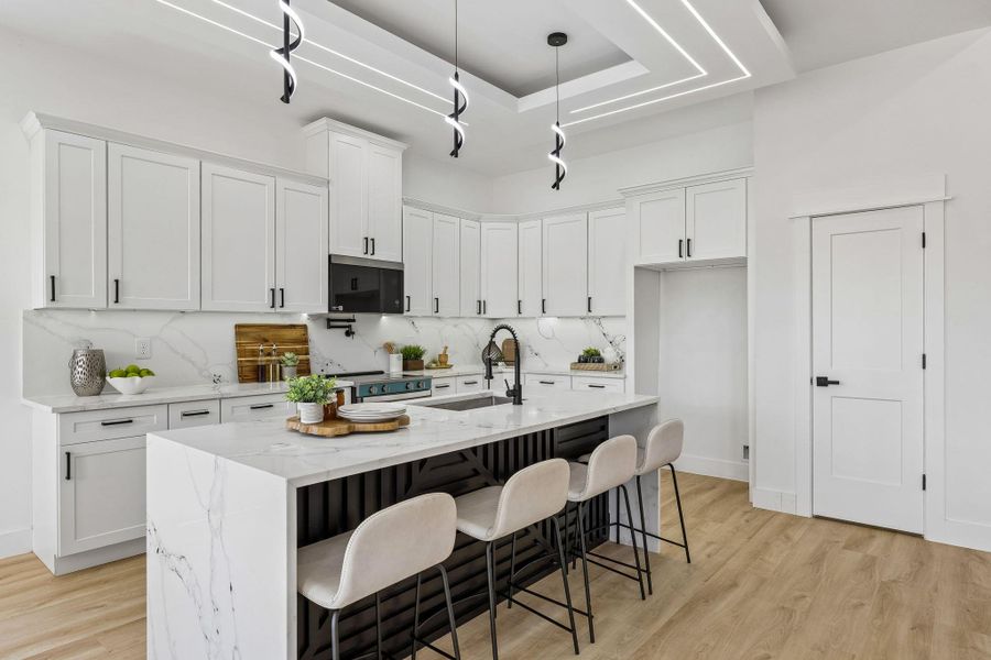 A waterfall stone island and detailed tray ceiling anchor this modern kitchen workspace.
