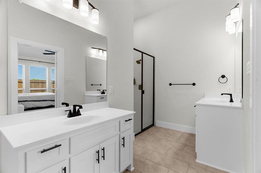 Ensuite bathroom featuring two vanities, a stall shower, tile patterned floors, and baseboards Ensuite bathroom featuring two vanities, a stall shower, tile patterned floors, and baseboards