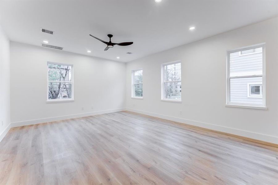 This spacious living room features an open layout with light wood flooring, modern decor, and ample natural light from large windows, ceiling fan, and recessed lighting.