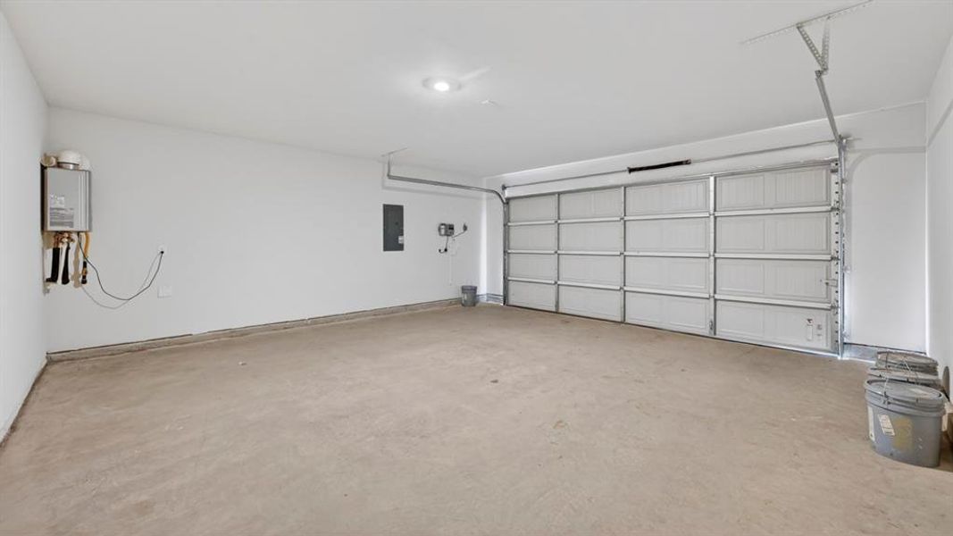 Spacious garage featuring a concrete floor, bright overhead lighting, a tankless water heater, and an electrical panel