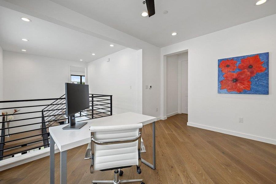 Open loft area featuring wood-finish flooring, recessed lighting, and a contemporary black metal staircase railing