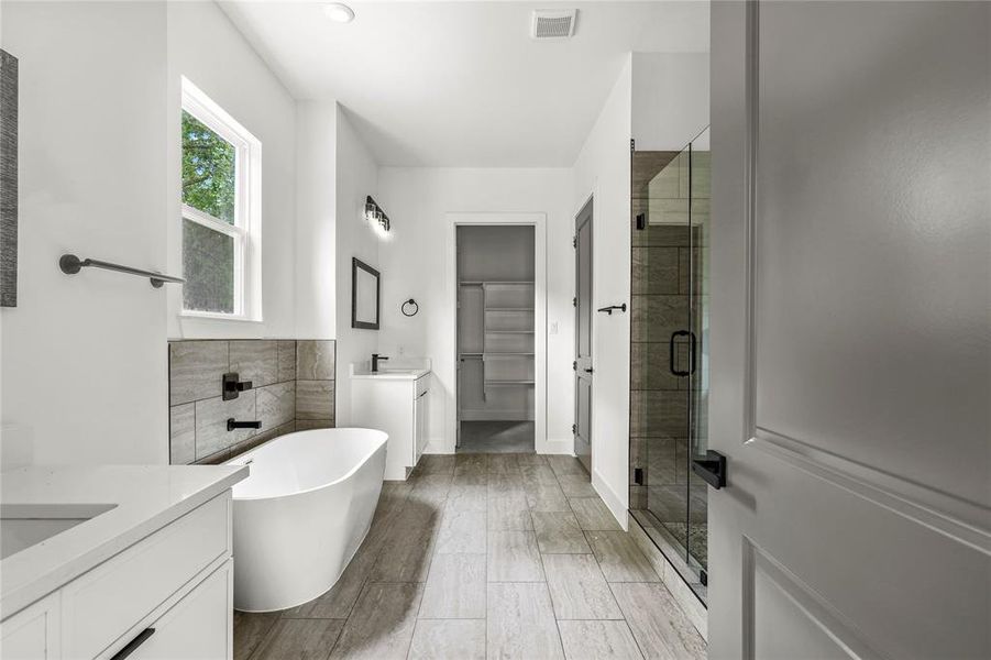 Full bath with two vanities, a shower stall, and a soaking tub