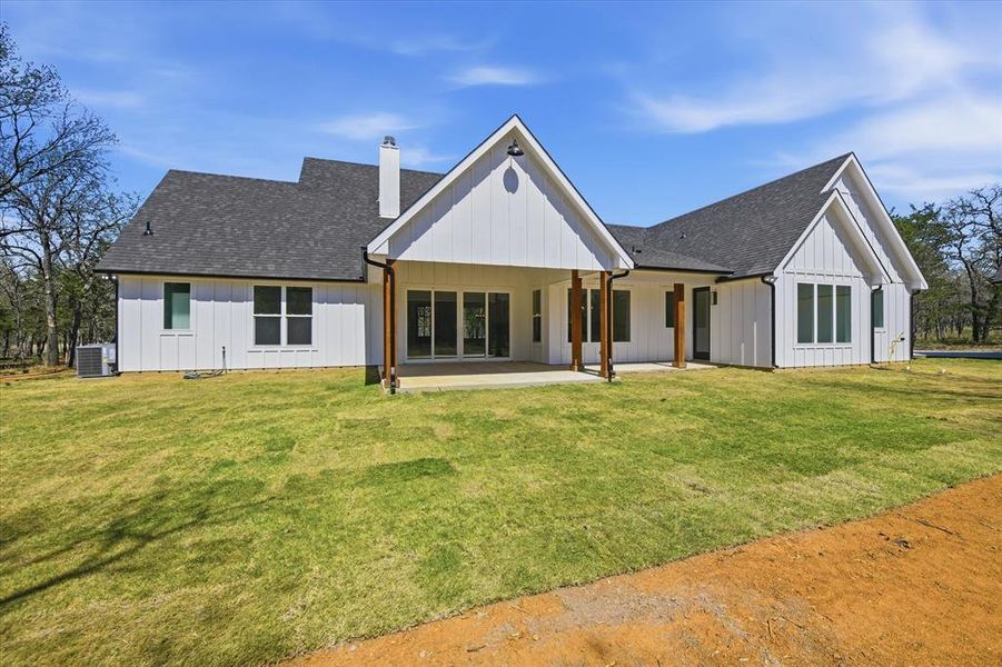 Back of house featuring roof with shingles, a chimney, a yard, and board and batten siding