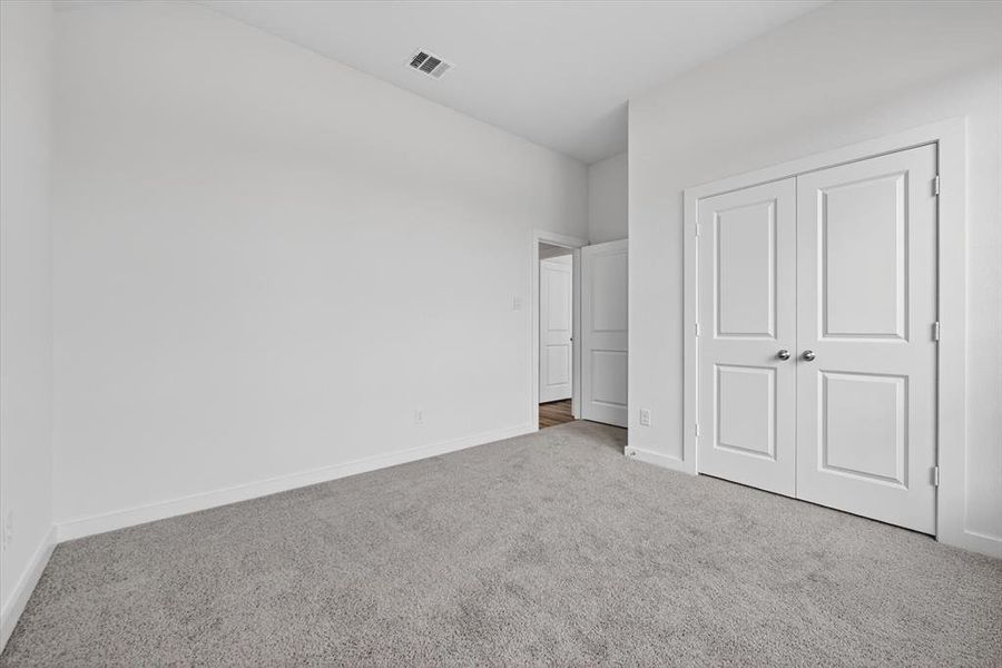 Neutral toned walls with white baseboards, gray carpeting, and a double-door closet with polished chrome hardware