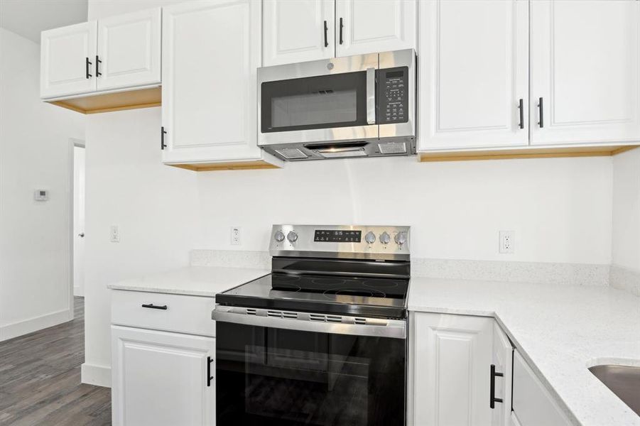 Kitchen with baseboards, white cabinetry, stainless steel appliances, and wood finished floors