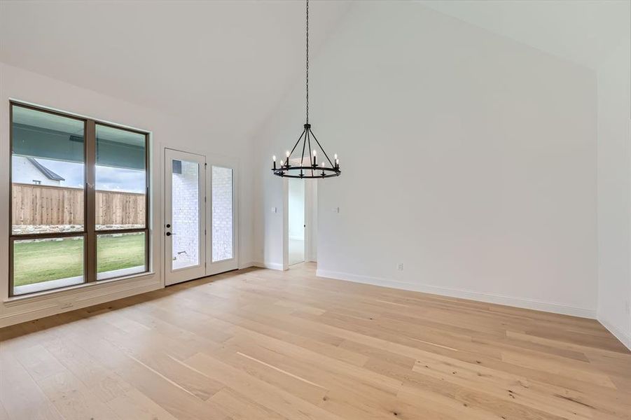 Unfurnished dining area featuring light hardwood / wood-style floors, an inviting chandelier, and high vaulted ceiling