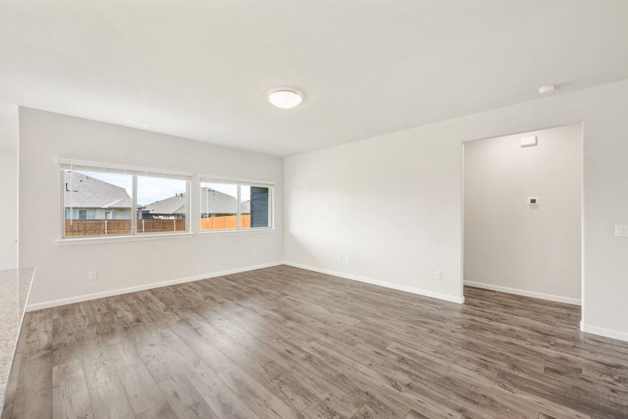 Empty living room with gray wood-look floors, white walls, and a large window overlooking the backyard