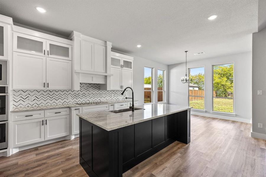 Kitchen with dark cabinetry, white cabinets, glass insert cabinets, decorative light fixtures, and recessed lighting