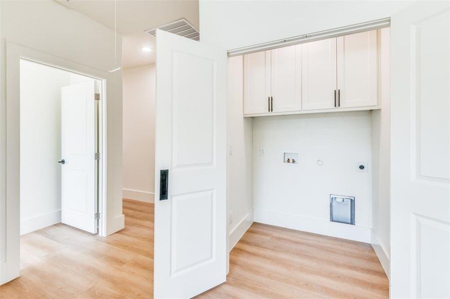 Washroom with hookup for a gas dryer, hookup for an electric dryer, light hardwood / wood-style floors, washer hookup, and cabinets