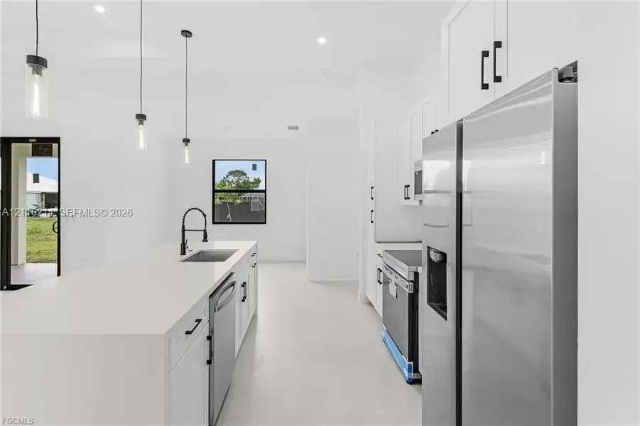 Kitchen featuring a central island with a solid surface countertop, stainless steel appliances, white cabinetry with matte black hardware, and pendant lighting