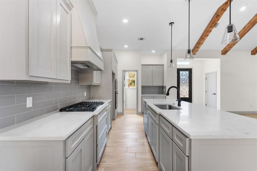 Kitchen featuring a center island with sink, light stone countertops, pendant lighting, beamed ceiling, and backsplash