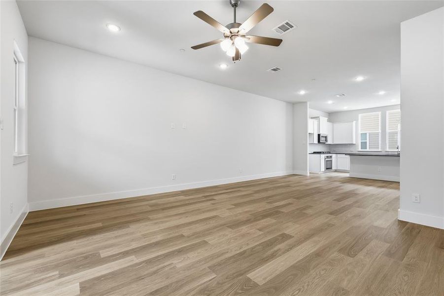 Spacious living area featuring light-toned flooring, recessed lighting, and a ceiling fan