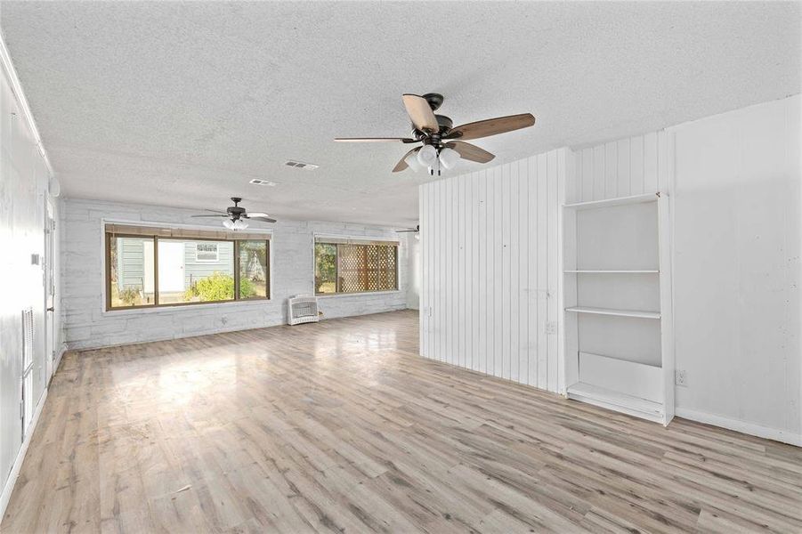 Unfurnished living room with light wood-style flooring, a textured ceiling, and built in features
