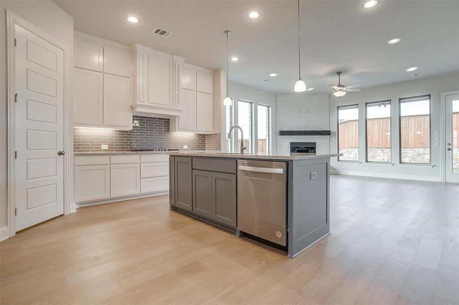 Kitchen featuring tasteful backsplash, white cabinets, stainless steel appliances, light hardwood / wood-style floors, and a fireplace