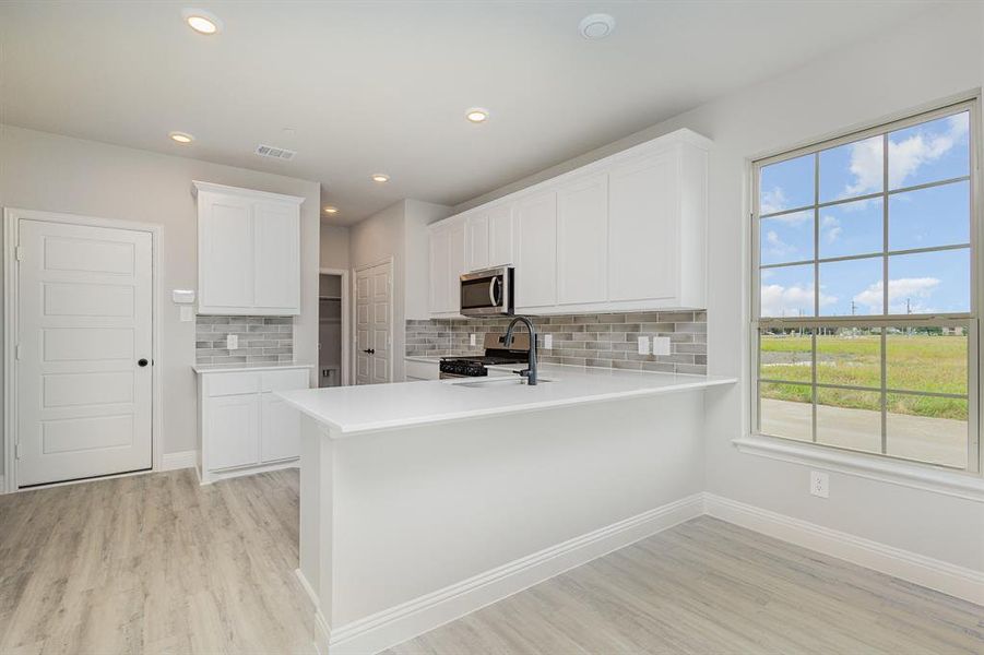 Kitchen with tasteful backsplash, light countertops, light wood finished floors, and recessed lighting