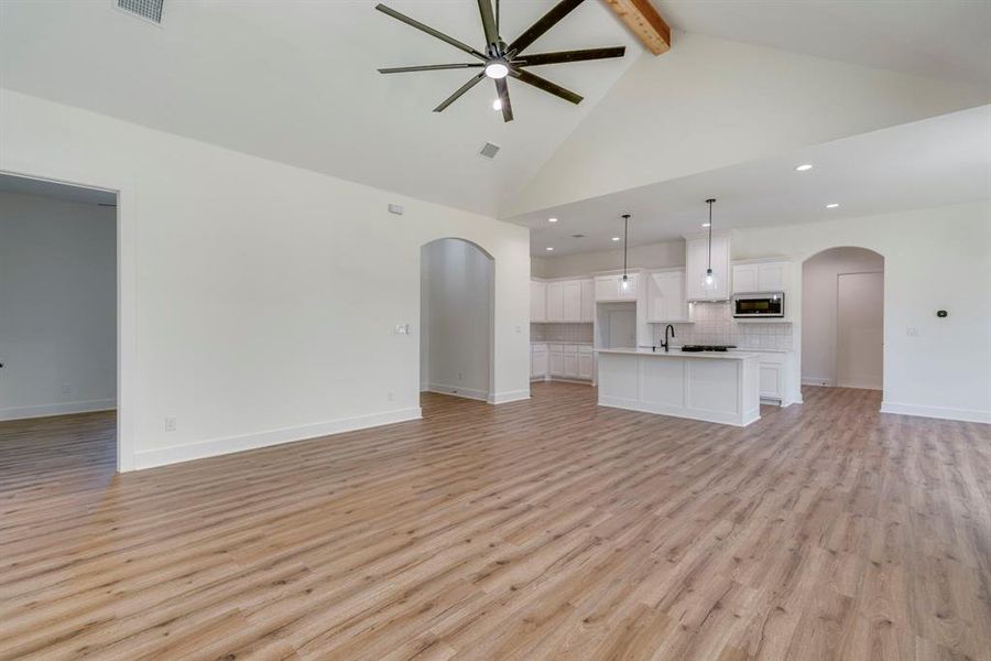 Unfurnished living room with beamed ceiling, light hardwood / wood-style floors, sink, high vaulted ceiling, and ceiling fan