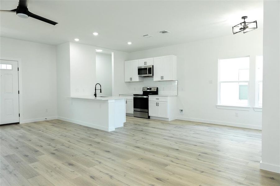 Kitchen featuring kitchen peninsula, stainless steel appliances, light wood-type flooring, white cabinets, and sink