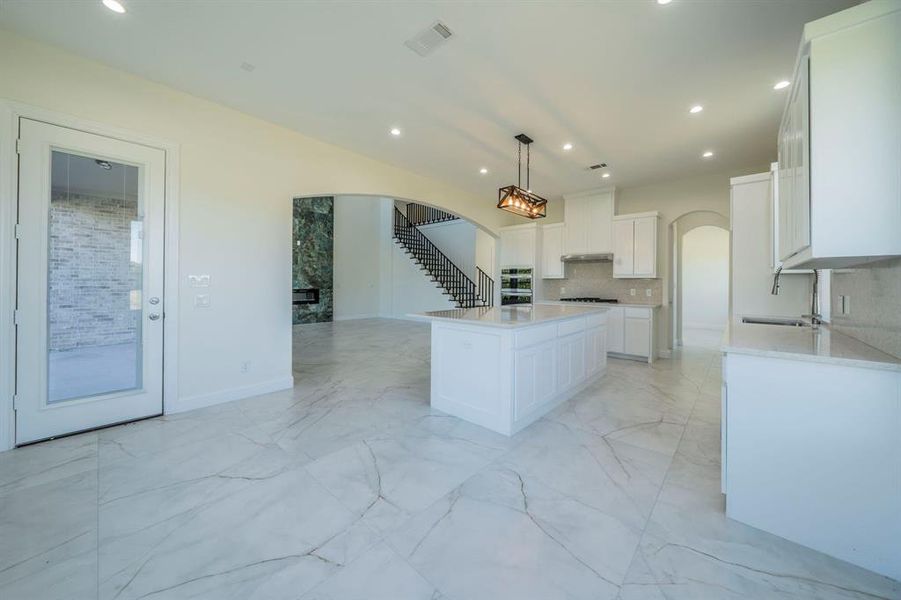 Kitchen with light stone counters, light marble finish floors, white cabinets, decorative light fixtures, and recessed lighting Kitchen with light stone counters, light marble finish floors, white cabinets, decorative light fixtures, and recessed lighting