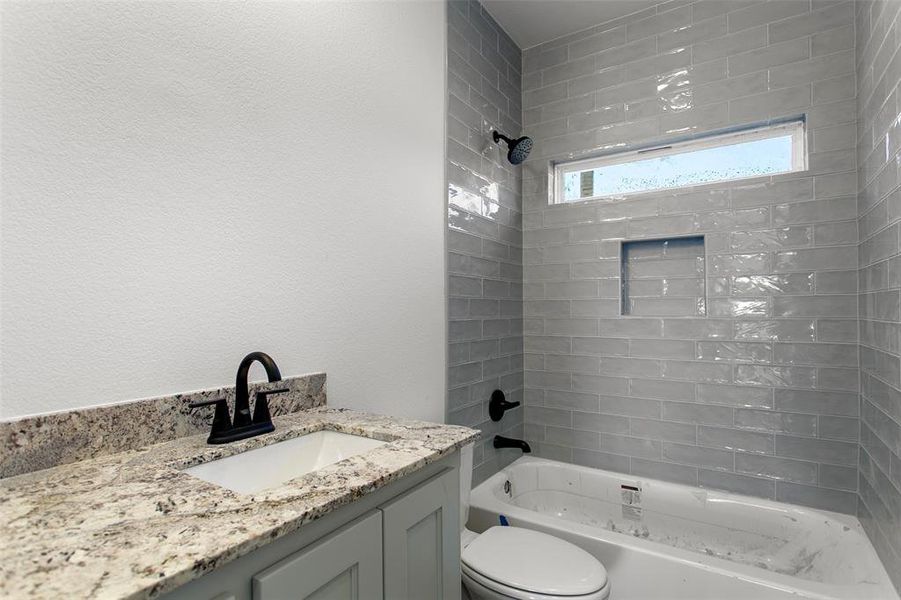 Full bathroom featuring vanity, tiled shower / bath combo, and toilet