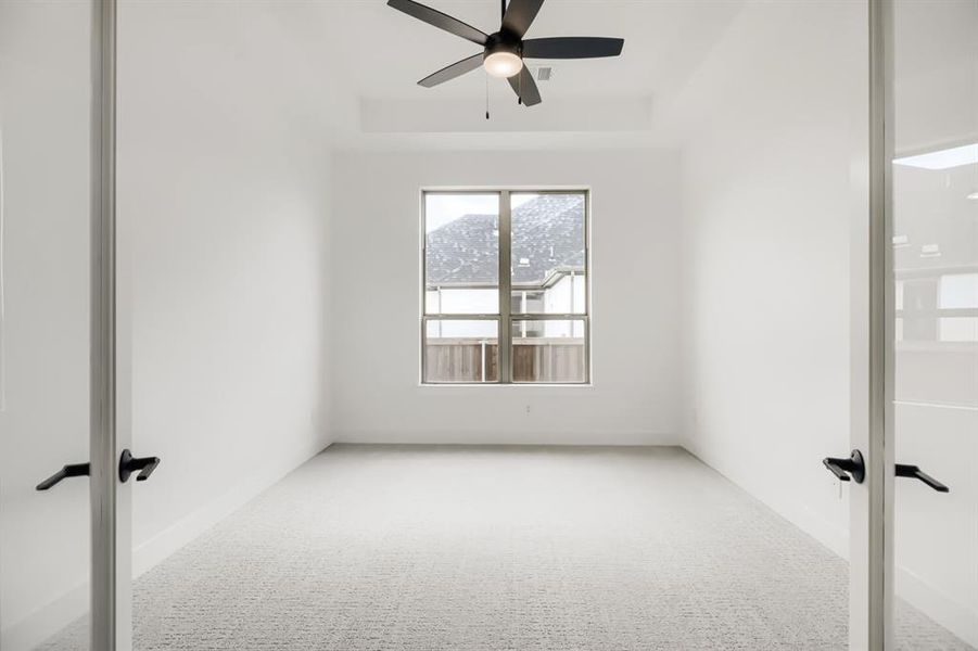 Carpeted spare room featuring a raised ceiling, ceiling fan, and french doors
