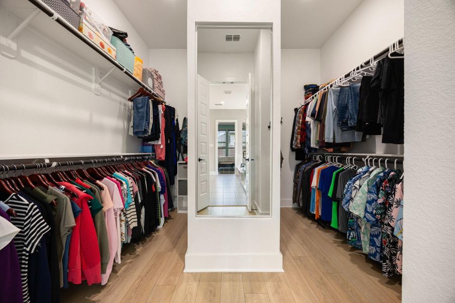 Spacious walk-in closet featuring dual hanging racks on both sides, built-in shelving, and a center divider for additional storage options. The open layout offers ample space for organization while the wood-look flooring and bright walls create a clean, polished look.
