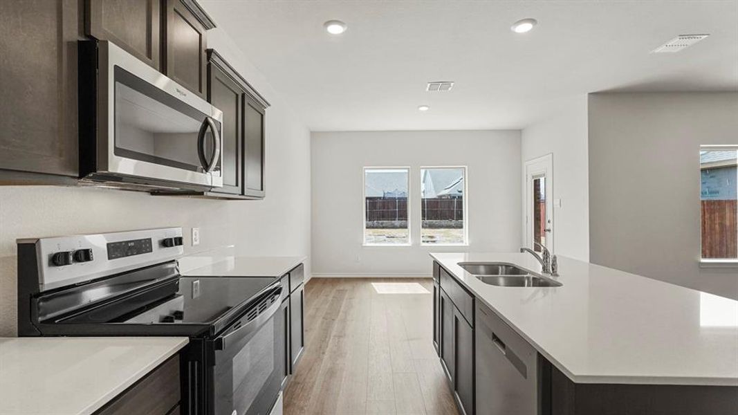 The kitchen features dark wood cabinetry, white countertops, and stainless steel appliances including a microwave and range