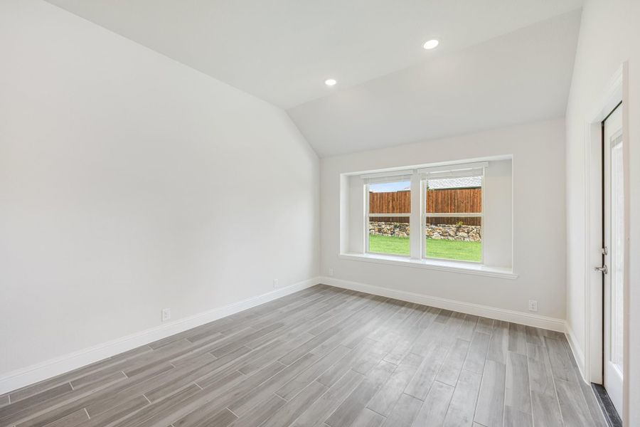 Empty room with vaulted ceiling, gray wood-look floors, and a window overlooking a fenced backyard Empty room with vaulted ceiling, gray wood-look floors, and a window overlooking a fenced backyard