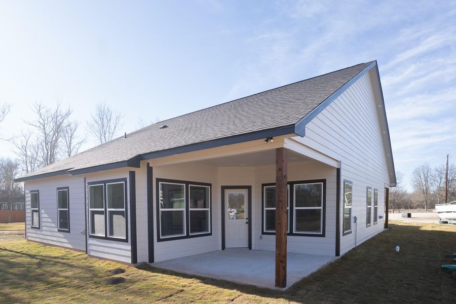 Rear view of house featuring a lawn, a patio area, and a shingled roof