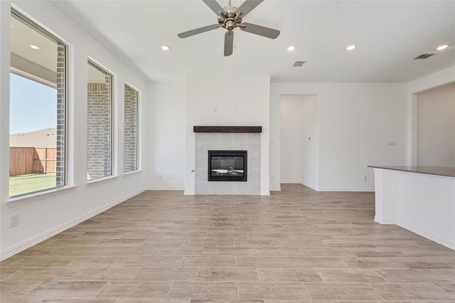 Unfurnished living room with ceiling fan, light wood-type flooring, and a tile fireplace