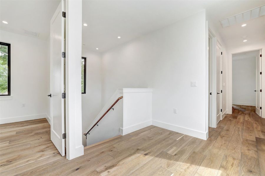 Corridor with an upstairs landing, light wood-style flooring, plenty of natural light, and recessed lighting Corridor with an upstairs landing, light wood-style flooring, plenty of natural light, and recessed lighting