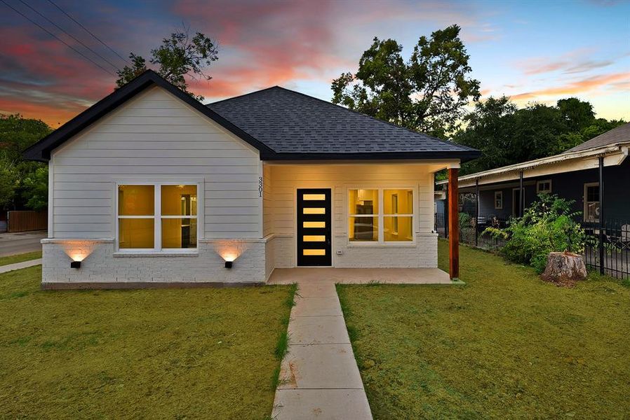 Rear view of property featuring a lawn, roof with shingles, covered porch, and brick siding