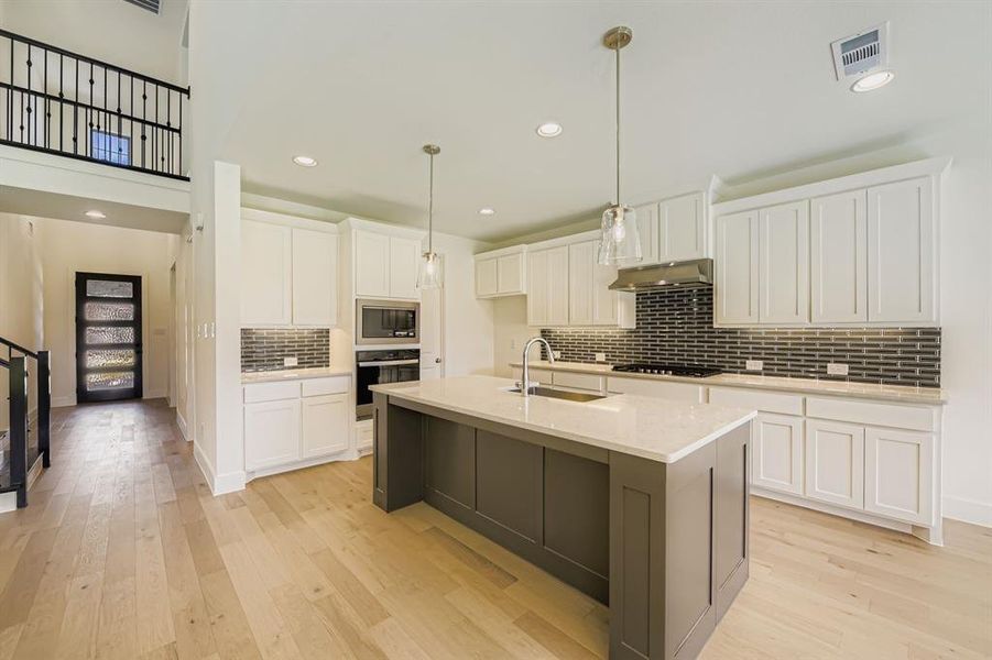 Kitchen with white cabinets, tasteful backsplash, decorative light fixtures, light wood finished floors, and recessed lighting Kitchen with white cabinets, tasteful backsplash, decorative light fixtures, light wood finished floors, and recessed lighting