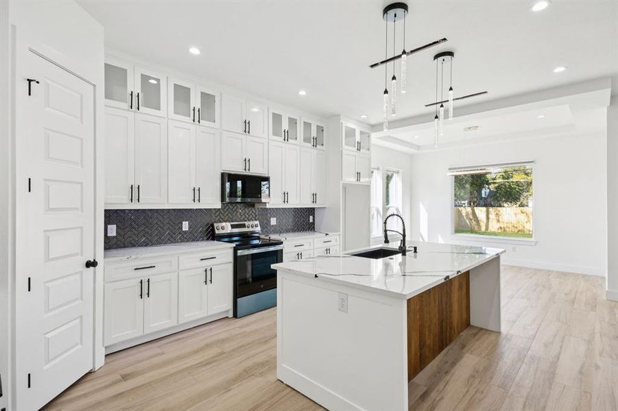 Kitchen with appliances with stainless steel finishes, light stone countertops, tasteful backsplash, a center island with sink, and glass insert cabinets