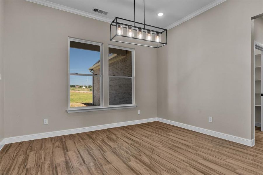 Unfurnished dining area with crown molding, wood finished floors, and a chandelier Unfurnished dining area with crown molding, wood finished floors, and a chandelier