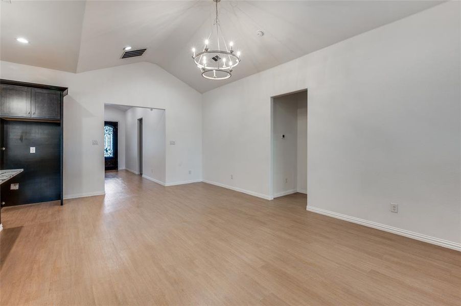 Unfurnished living room featuring light wood-type flooring, an inviting chandelier, and vaulted ceiling