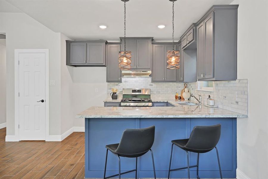 Kitchen with dark hardwood / wood-style floors, gray cabinetry, hanging light fixtures, and stainless steel gas range