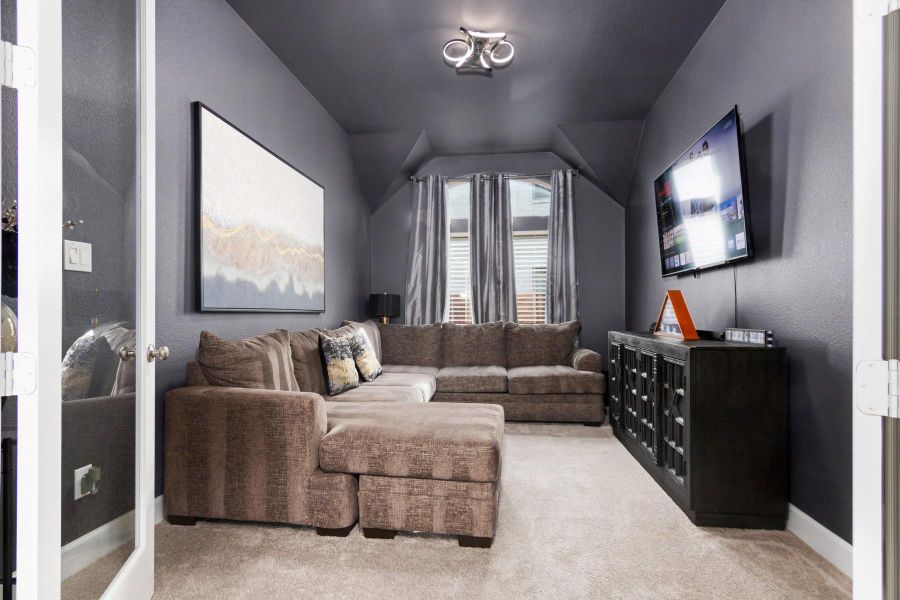 This cozy media room features modern lighting fixture. The dark walls and carpet create an inviting, intimate atmosphere, while large windows with curtains offer natural light.