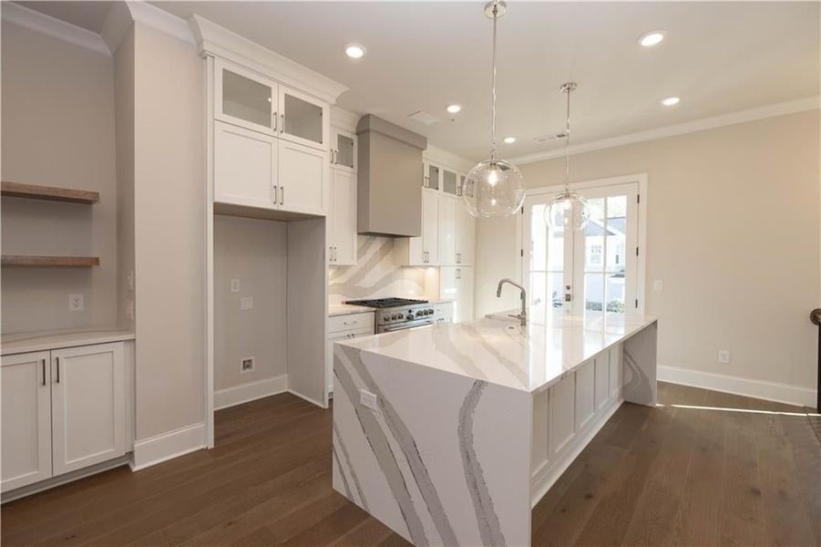 Kitchen featuring ornamental molding, glass insert cabinets, white cabinets, dark wood finished floors, and an island with sink