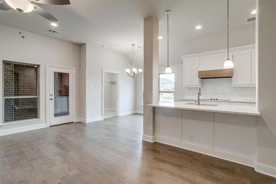 Kitchen featuring ceiling fan with notable chandelier, light stone countertops, hardwood / wood-style floors, hanging light fixtures, and white cabinets