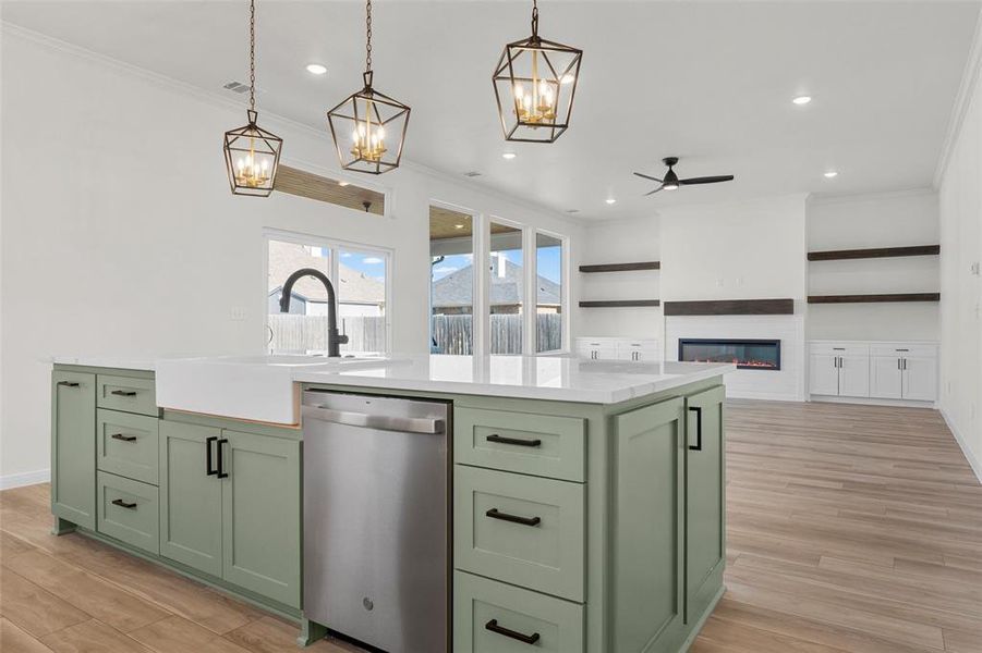 Kitchen featuring green cabinets, a center island with sink, crown molding, dishwasher, and a glass covered fireplace