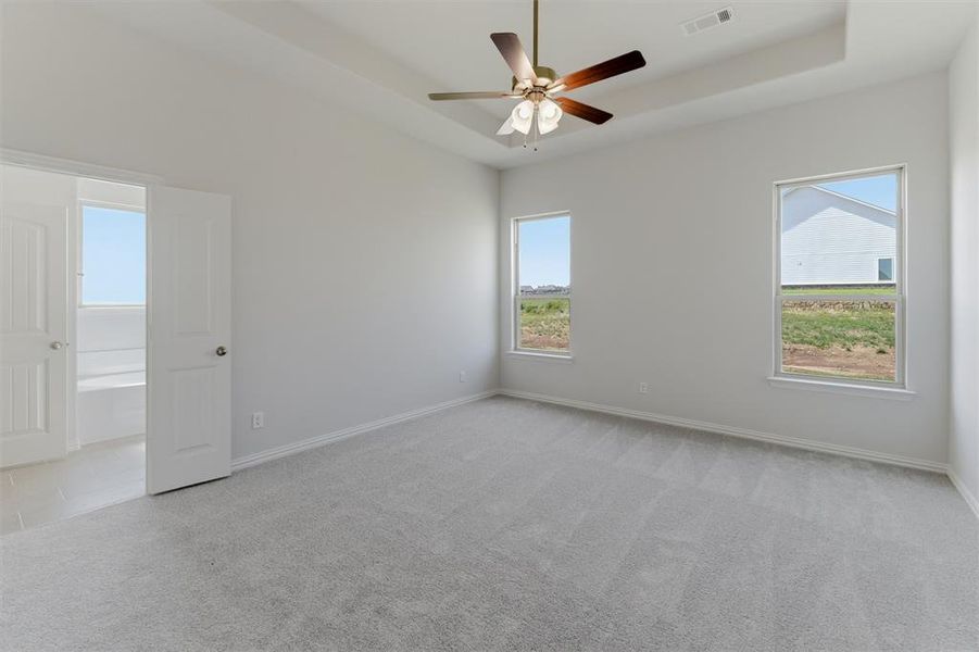 Spacious room featuring light gray carpeting, a tray ceiling with a ceiling fan, and two large windows