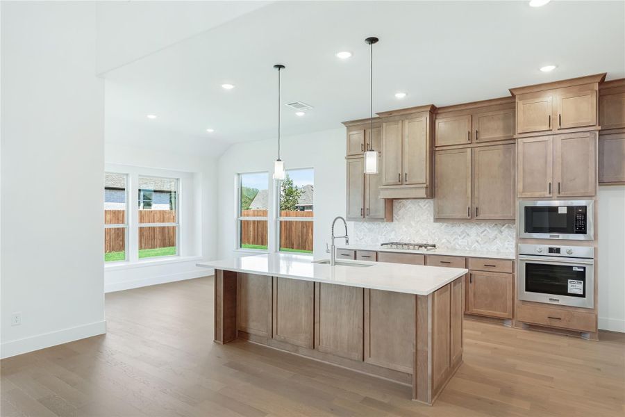 Kitchen with large center island, wood cabinets, herringbone backsplash, and stainless steel double oven