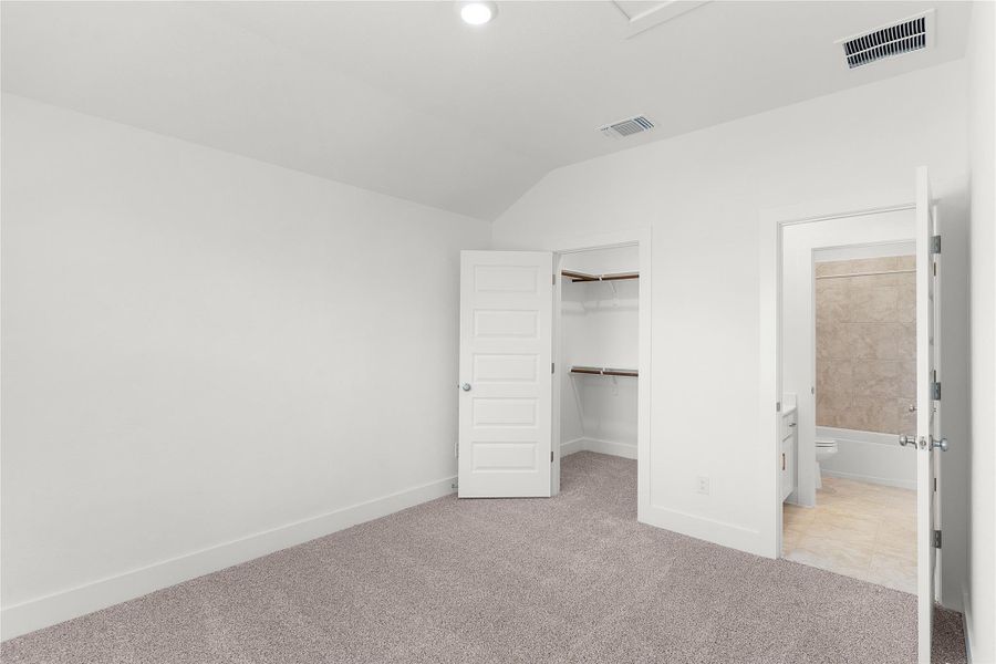 Unfurnished bedroom with light colored carpet, a spacious closet, vaulted ceiling, and ensuite bathroom