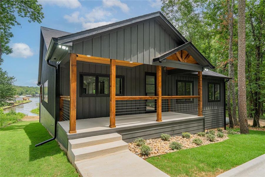 View of front of home with board and batten siding, covered porch, a water view, and a front lawn View of front of home with board and batten siding, covered porch, a water view, and a front lawn