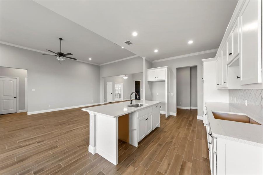 Kitchen with white cabinetry, ceiling fan, sink, crown molding, and a center island with sink