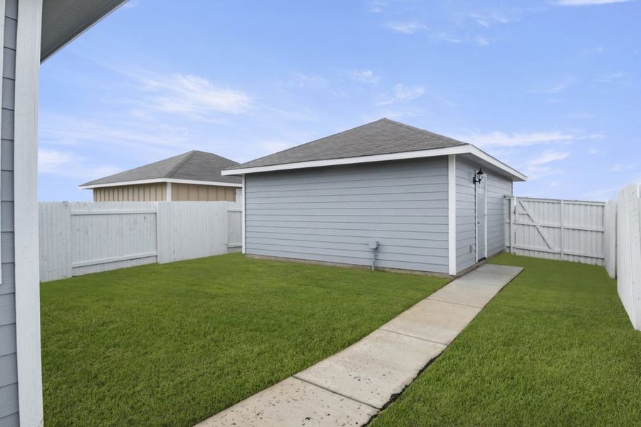 Image of back exterior of a grey two car garage with a cement path and green grass with a white fence